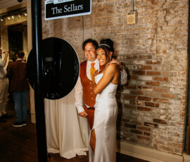 Couple in formal attire poses beneath The Sellars street sign in a warmly lit, exposed-brick New Orleans wedding venue.