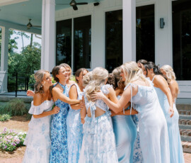 Women in light blue dresses hug and smile outside a building, capturing joyful Louisiana wedding inspiration.