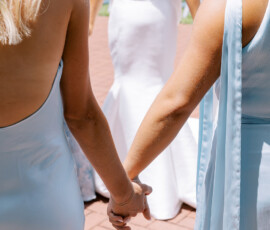 “Bride and bridesmaids holding hands in a prayer circle before the outdoor wedding ceremony, wearing white and light blue dresses.”