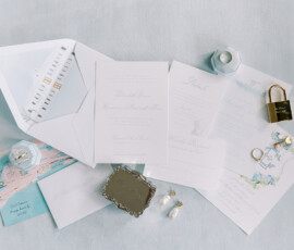 Flat lay of wedding stationery with invitations, RSVP cards, rings, and decor on a light blue surface for Louisiana weddings.