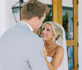 Bride in white dress and veil embraces groom in light gray suit before wooden doors at their New Orleans wedding.