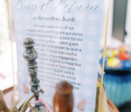 Ring & Return“ sign at a Louisiana wedding with antique brass bells and pink ribbons arranged on a table.