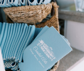 Basket of light blue Coastal Arts, Ocean Beach, Alabama drink koozies, neatly stacked for a wedding or reception.