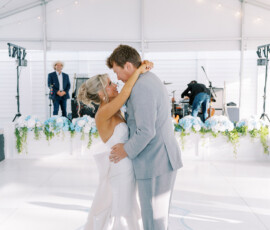 Bride and groom share their first dance in a white tent with blue flowers and string lights at an elegant Gulf South wedding.