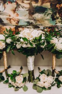 Bridal bouquet of white roses and greenery with matching bouquets in front of a soft-toned classical painting, New Orleans wedding.