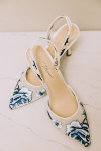 White slingback heels with blue floral embroidery on marble—ideal shoes for a New Orleans wedding ceremony.
