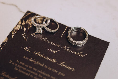 Three silver rings on a brown wedding invite with gold script for Mr. Sherman Hannibal and Ms. Antoinette Turner.