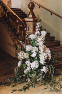 White and pale pink floral arrangement with greenery decorates a rustic wooden staircase, perfect for an elegant Louisiana wedding.