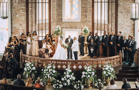 Bride and groom with wedding party at a formal Louisiana church ceremony, surrounded by guests and lush floral decor.