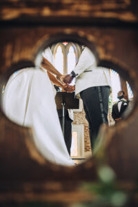 Bride and groom holding hands at their Gulf South wedding, seen through wooden decor, with a groomsman in the background.