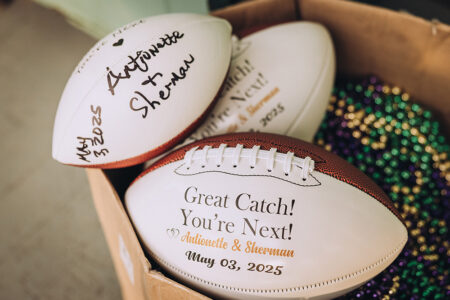 Gift box with two personalized footballs, a third football, and colorful bead necklaces for New Orleans wedding inspiration.