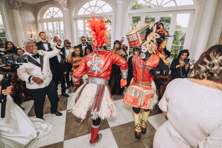 Two guests in red traditional costumes dance at a lively indoor Gulf South wedding, as formally dressed guests cheer nearby.