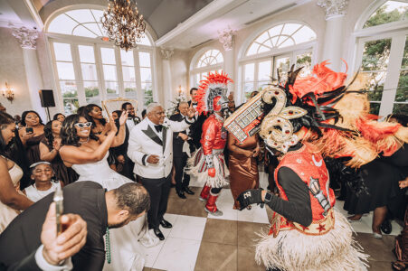 Bride in white dress and sunglasses enjoys vibrant Louisiana wedding as feathered performers entertain dancing guests.