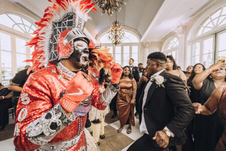 Performer in sparkling costume and feathered headdress entertains at a lively Louisiana-inspired indoor wedding celebration.