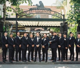 Men in black tuxedos pose under the Musical Legends Park sign in New Orleans, showcasing wedding inspiration.