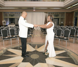 A couple in white formalwear dances, smiling, on a starburst floor in an elegant empty hall—classic New Orleans wedding style.
