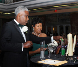 A couple pours colored sand into a vase at a candlelit Louisiana wedding ceremony, watched by guests.