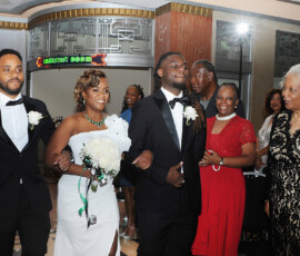 Bride in white dress and two men in tuxedos walk down the aisle, smiling at a classic New Orleans wedding ceremony.