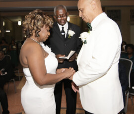 Bride and groom exchange rings with officiant at a formal New Orleans wedding; guests seated in the background.