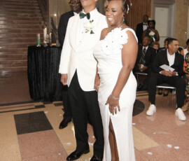 Smiling couple in formal white at indoor event, with guests and marble stairs—classic New Orleans wedding elegance.