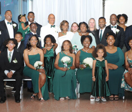 Formally dressed in green and black, a group smiles for a photo at an elegant Gulf South wedding, seated and standing together.
