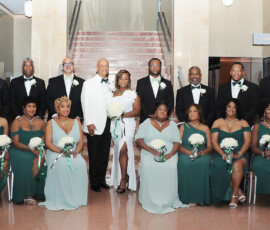 Indoor wedding party with bride, groom, guests in green dresses and black tuxedos, all smiling for a Gulf South celebration.