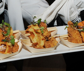 Server presents a white tray with four garnished mini chicken sandwiches in wooden dishes, ideal for wedding receptions.