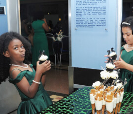 Two girls in green dresses holding cupcakes, smiling at a lively Louisiana wedding dessert table with parfaits and guests mingling.