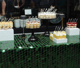 Layered desserts in clear cups with spoons on a green tablecloth, perfect for a Louisiana wedding dessert table.
