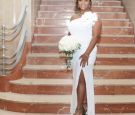 Smiling woman in white dress with short curly hair holds white roses on marble stairs at a joyful Louisiana wedding.