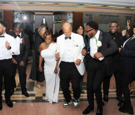 Formally dressed guests dance and smile at a lively Louisiana wedding reception in a decorated hall with patterned floors.