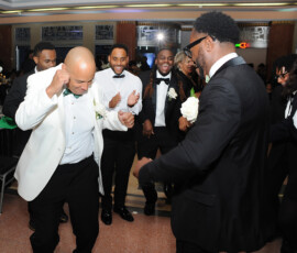 Men in tuxedos dance together at a formal event, led by one in a white jacket—timeless New Orleans wedding inspiration.