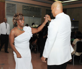 A woman in a white dress dances with a bald man at a formal New Orleans wedding, with guests celebrating in the background.