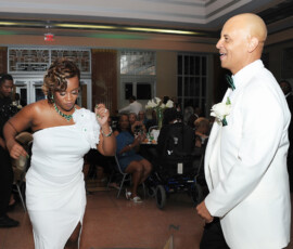 Bride in a white dress and groom in a white suit dance at an indoor Gulf South wedding as guests watch.
