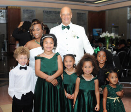 Formally dressed family in coordinated green and white outfits pose at a joyful Louisiana wedding reception.