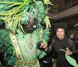 Person in green feathered costume with face paint stands by a smiling woman in black at a unique wedding inspiration event.