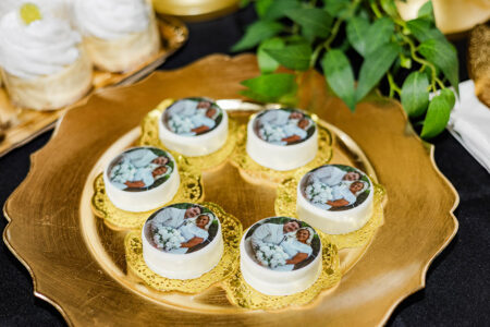 Six white desserts with a couple’s photo on a gold plate, surrounded by green leaves and sweets at a New Orleans wedding.