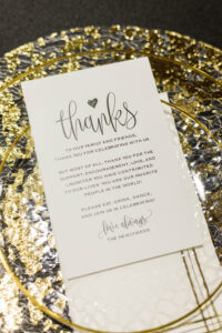 White wedding thank-you card on a clear and gold plate, featuring elegant script and printed text for New Orleans weddings.