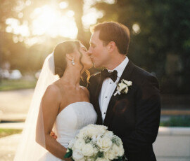 Bride and groom kiss at sunset in the Gulf South, with her in a strapless gown and him in a black tuxedo.