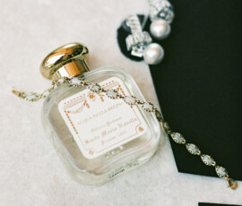 Elegant flatlay with a gold-capped perfume bottle, jewelry, black envelope, and Rehearsal Dinner card for a Louisiana wedding.