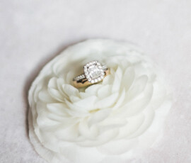 Diamond halo engagement ring on layered white flower atop a pale pink surface—perfect for a romantic Louisiana wedding.