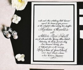 Elegant black and white wedding invitations, pearl earrings, flowers, and envelopes arranged neatly on a light surface.