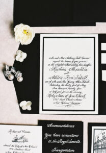 Elegant black and white wedding invitations, pearl earrings, flowers, and envelopes arranged neatly on a light surface.