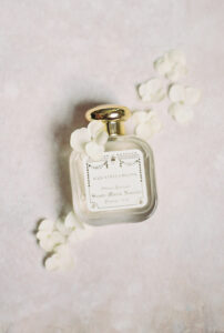 Acqua Della Regina perfume bottle with gold cap and white petals on a soft background, ideal for elegant Louisiana weddings.