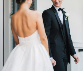 Bride in white gown and groom in tuxedo smile outside near white walls and green shutters at a New Orleans wedding.