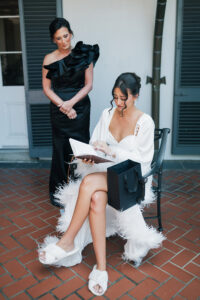 Bride in a robe reads a letter, emotional, with bridesmaid beside her on a New Orleans patio before the wedding.