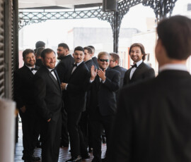 Men in black tuxedos smile on a covered walkway at a Gulf South wedding, offering timeless ceremony inspiration.