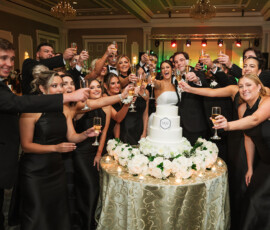 Guests in formalwear toast around a decorated wedding cake with white flowers at an elegant Louisiana wedding reception.
