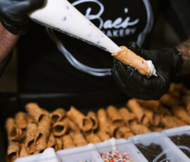 A person in black gloves fills a cannoli with cream; sprinkles and chocolate chips sit nearby for New Orleans wedding treats.