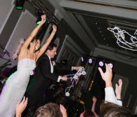 Bride and groom celebrate on stage with raised arms as guests toss white streamers at their Gulf South wedding reception.